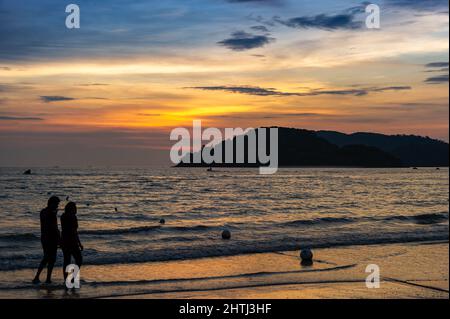 Chenang Beach at Sunset mit einem Paar, das im Vordergrund auf Langkawi Island spazierengeht Stockfoto