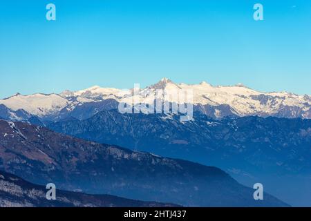 Die Bergkette des Monte Baldo, das Etschtal und der Nationalpark Adamello Brenta mit dem Gipfel des Care Alto von der Lessinia-Hochebene aus gesehen. Italien. Stockfoto