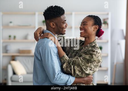 Liebevolle schwarze Familie militärische Frau und Mann umarmt zu Hause Stockfoto