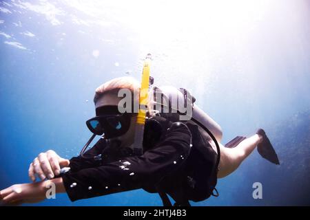 Zeit zum Abstieg. Junge Taucherin schwimmt durch das Wasser, während sie ihren Tauchcomputer überprüft - Copyspace. Stockfoto