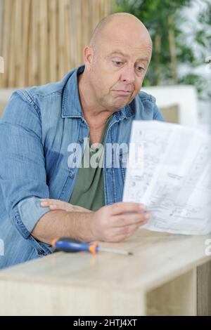 frustriert Mann Anleitung lesen und Zusammenstellung Selbstmontage Möbel Stockfoto