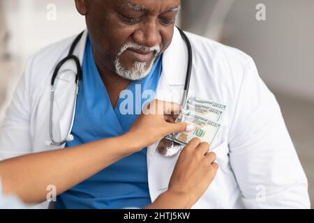 Schwarze weibliche Hand, die Geld in die Tasche des Arztes legt Stockfoto