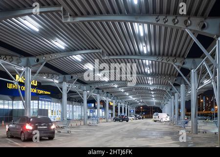 Moskau. Russland. 25. Februar 2022. Nachts ist der Parkplatz in der Nähe des METRO-Hypermarktes halb leer. Hell erleuchteter Parkplatz unter einem Vordach in der Nähe des METRO-Einkaufszentrums. Stockfoto