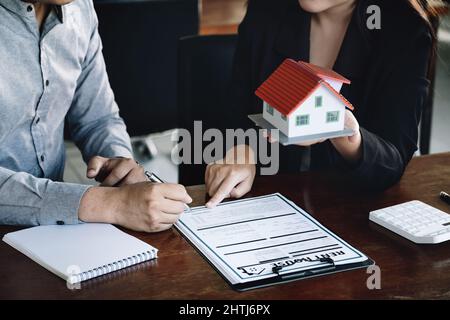 Konzept der Unterzeichnung Darlehen, Refinanzierung, Kauf von Haus und Land, Mietunterkünfte, männliche Kunden Unterzeichnung Vertrag mit weiblichen Immobilienmakler zu kaufen Stockfoto