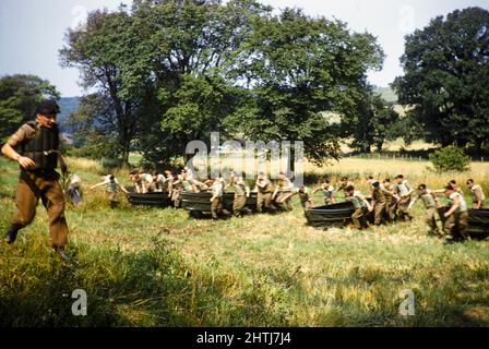 Schüler, die als Armeekader militärische Trainingsübungen machten, Südengland, Großbritannien, Ende 1950s mit Booten über ein Feld Stockfoto