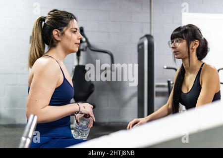 Zwei junge Frauen, die sich im Fitnessstudio entspannen und unterhalten. Gesunder Lebensstil, Workout-Konzept Stockfoto
