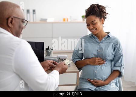 Reife erfahrene schwarze Arzt gibt Pillen zu schwanger Dame Stockfoto