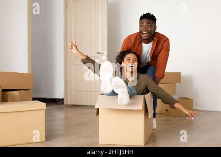 Happy African Man Riding Frau In Moving Box Zu Hause Stockfoto