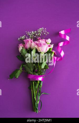 Blumenstrauß mit Bändchen und lila Rosen mit Eukalyptus auf violettem Hintergrund. Kopierbereich, Draufsicht. Stockfoto