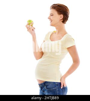 Gesunde Ernährung für das Baby. Eine Schwangere, die einen knusprigen grünen Apfel betrachtet, während sie auf weißem Hintergrund isoliert ist. Stockfoto