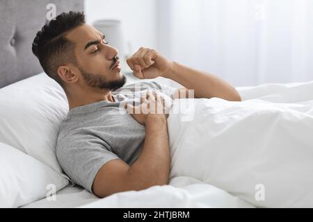 Kranker Junger Arabischer Mann Hustet, Während Er Zu Hause Im Bett Liegt Stockfoto