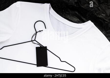 T-Shirt-Modell aus weißer Baumwolle. Platz für ein Logo oder ein Etikett, Nahaufnahme. Schwarzes Etikett auf einem Aufhänger. Stockfoto