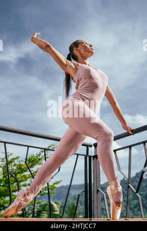 Junge Ballerina in Punkten, die sich strecken, auf Zehen stehend gegen den blauen Himmel Stockfoto