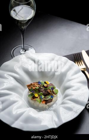 Appetitliche Snacks mit Meeresfrüchten, in der Nähe dekoriert mit knusprigem Gemüse auf schwarzem Hintergrund und Besteck im Restaurant Stockfoto