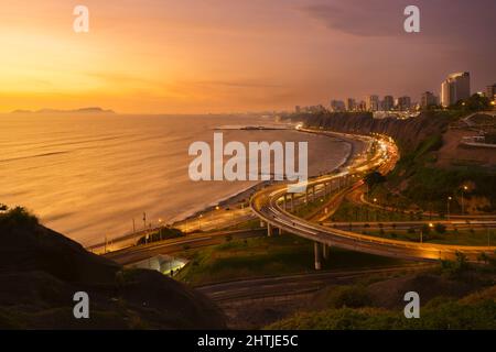 Lange Exposition der glühenden leeren Brücke in der Nähe des Meeres an der Küste der Küstenstadt mit Wohngebäuden am Abend Stockfoto