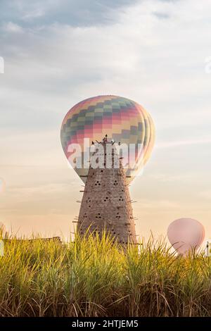 Hoher konischer Nesttaubenturm mit vielen Löchern auf grasbewachsenem Feld mit Luftballons in Ägypten am Sommertag Stockfoto