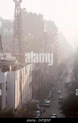 Autos fahren auf einer geraden asphaltierten Straße entlang hoher Wohngebäude auf einer Straße mit grünen Bäumen gegen den wolkenlosen Himmel in Ägypten Stockfoto