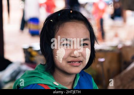 Kakku, Myanmar - 04.16.2017 - PaO Teenager-Mädchen mit weißer Tanaka-Kosmetikpaste auf dem lokalen Straßenbasar im Dorf und schaut in die Kamera Stockfoto