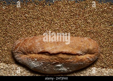 Draufsicht Vollformat von frischem, gesund gebackenem Brot auf rohem Buchweizen und Haferkörnern in hellem Raum gelegt Stockfoto