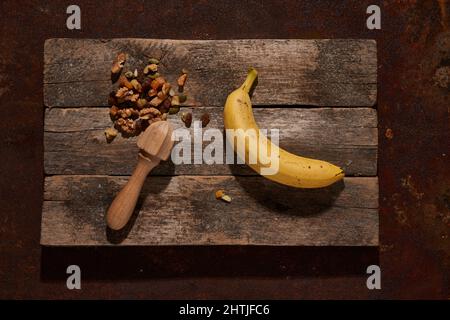 Draufsicht auf ganze reife Banane und getrocknete Früchte und Nüsse auf rostigen Tisch auf Holz Schneidebrett gelegt Stockfoto