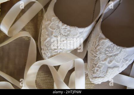 Draufsicht auf elegante weiße Hochzeitsschuhe mit Stickerei, die während der Feiertagsfeier auf dem Boden mit weißem Band im hellen Raum platziert sind Stockfoto