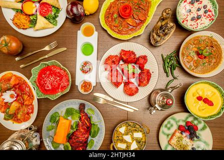 Set von indischen Gerichten mit Chicken Tikka Masala in der Mitte, Fleisch gefüllte Samosas, rotes Korma, Zimtstangen, pilau-Reis und mehr Gewürze Stockfoto