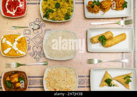 Draufsicht auf eine Reihe von indischen Gerichten, mit Pilau-Reis, Gemüsesamosen, rotem Korma und Zwiebeln Stockfoto