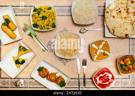 Set von indischen Gerichten mit Pilau-Reis, Gemüsesamosen, rotem Korma und Zwiebeln Stockfoto