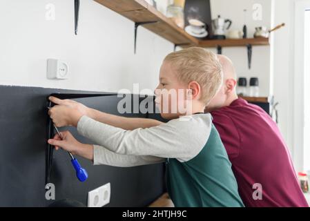 Vater und Sohn machen gemeinsam Hausrenovierungen. Mit Schraubendreher. Vater lehrt Kind Werkzeuge zu verwenden Stockfoto