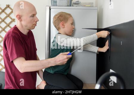 Vater und Sohn machen gemeinsam Hausrenovierungen. Mit Schraubendreher. Vater lehrt Kind Werkzeuge zu verwenden Stockfoto