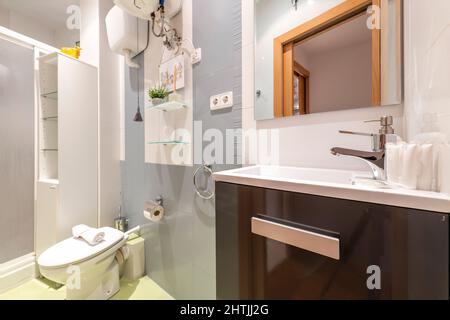 Badezimmer mit dunklen Holzmöbeln, rahmenlosem Glasspiegel über weißem Porzellanwaschbecken und Duschkabine im Hintergrund Stockfoto