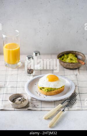 Frühstück Toast mit Avocado und sonniger Seite nach oben Ei. Gesundes Frühstück mit Avocado-Toast und Orangensaft Stockfoto