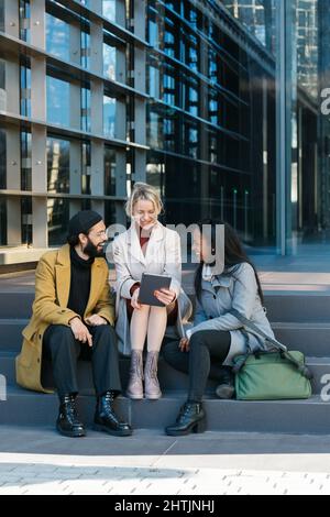 Geschäftskollegen, die ein digitales Tablet nutzen und über neue Projekte sprechen, während sie draußen auf einer Treppe sitzen. Stockfoto