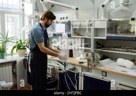 Arbeiter der Manufaktur, die weißes Blatt auf das Werkstück der prothetischen Fassung setzt, um seine Form vom Arbeitsplatz zu bilden und zu fixieren Stockfoto