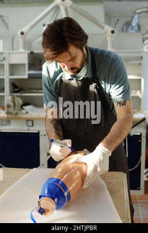 Männliche Arbeiter der prothetischen Fabrik in Handschuhen und Schürze schreiben auf Silikonlinie mit blauem Marker beim Biegen über den Arbeitsplatz Stockfoto