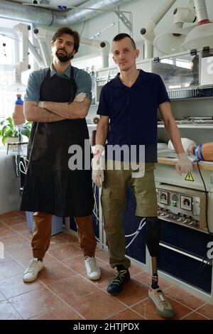 Junge Mitarbeiter der modernen prothetischen Fabrik stehen am Arbeitsplatz mit Werkstücken aus künstlichen Gliedmaßen und Gipsabgüssen Stockfoto