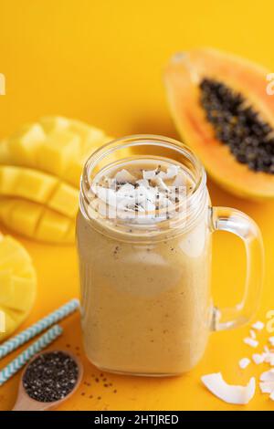 Köstlicher Mango-Kokosnuss-Smoothie, ein Getränk aus tropischen Früchten im Glas auf gelbem Hintergrund Stockfoto