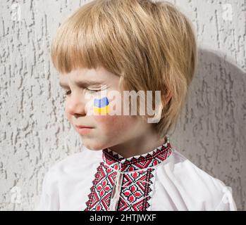 Boy's Face, die ukrainische Flagge ist auf der Wange mit gelben und blauen Farben bemalt. Russische Invasion der Ukraine, kein Krieg. Bitten Sie um Hilfe von der Welt c Stockfoto