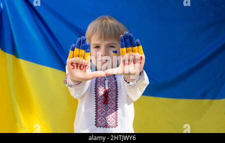 Junge in nationalen ukrainischen Kleidung legte seine Hände nach vorne, Inschrift STOP war vor dem Hintergrund der gelb-blauen Flagge. Russische Invasion der Ukraine, CH Stockfoto