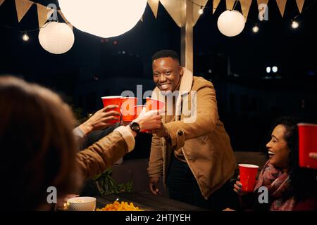 Schwarzer Mann steht, jubelt mit einer Gruppe von verschiedenen Freunden, die auf einer Party im Freien feiern Stockfoto