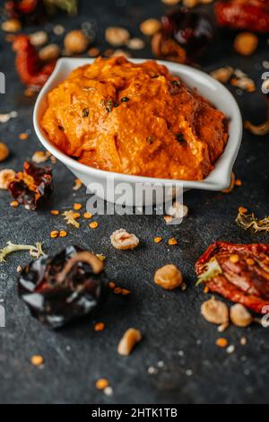 Eine weiße Keramikschale mit etwas Romesco-Sauce, typisch für Katalonien, Spanien, hergestellt mit Olivenöl, Knoblauch, Tomaten, Nyora-Pfeffer oder Haselnüssen, auf einem dunklen s Stockfoto