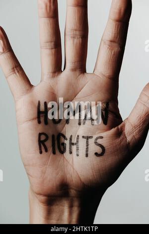 Nahaufnahme der Hand eines Mannes mit dem Text Menschenrechte in seiner Handfläche, auf einem cremefarbenen Hintergrund Stockfoto