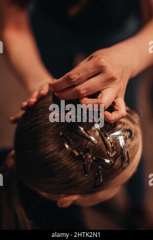 Weibliche Hände machen stilvolle Frisur auf Brünette Haare. Vertikale Modeaufnahme Stockfoto