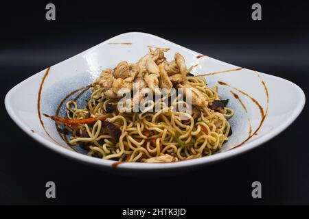 Gekochtes Huhn Yakisoba, asiatische Wok-Nudeln mit Huhn, Sesam, Teriyaki-Sauce und verzehrfertiges Gemüse. Studio Foto mit schwarzem Hintergrund. Stockfoto