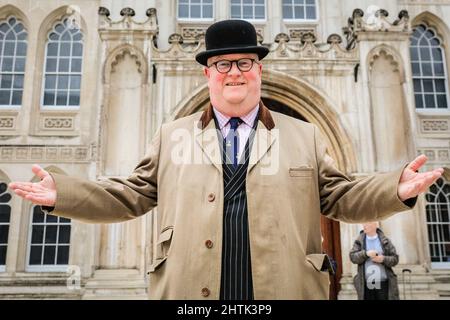 London, Großbritannien, 01.. März 2022. Der Ansager und Richter von der Worshipful Company of Poulters posiert in Melonenhut vor der Guildhall und beschließt, trotz heftigem Regen ein Lächeln auf den Lippen zu zaubern. Vertreter der Livreen der City of London und der worshipful Companies in ihren Regalien und ihren ausgefallenen Kleidern sind alle gekommen, um sich beim Inter Livery Pancake Race am Faschingsdienstag, auch gemeinhin als „Pancake Day“ bezeichnet, gegeneinander anzutreten. Das Rennen, jetzt in seinem 18. Jahr, findet immer im Guildhall Yard statt, wird aber in diesem Jahr auf einen zeremoniellen 'Wurf' reduziert, da der Regen rutschig ist. Kredit: Imageplotter Stockfoto