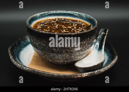 Original japanische Miso-Suppe, vegetarische Suppe mit Miso, Gemüse, Tofu und Sesam, serviert im Töpferservice auf schwarzem Hintergrund. Stockfoto