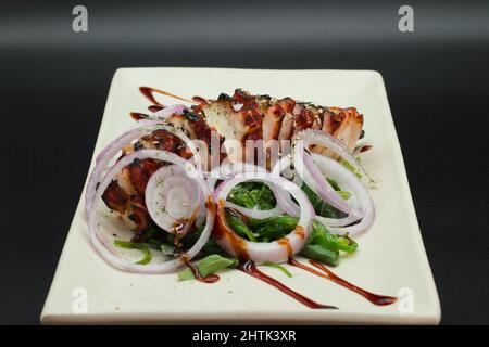 Japanischer Octopus Salat, frisch geschnittener Oktopus mit Algen, Zwiebeln und Teriyaki-Sauce. Fertigplatte serviert auf schwarzem Hintergrund vom japanischen Koch. Stockfoto