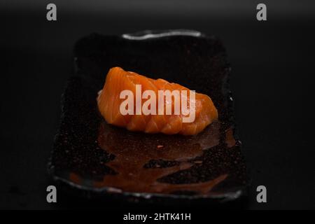 Traditioneller japanischer Sashimi Cut, Raw and Fresh Wildlamon aus Norwegen in Scheiben geschnitten und auf schwarzem Teller mit schwarzem Hintergrund auf minimalistische Weise serviert. Stockfoto