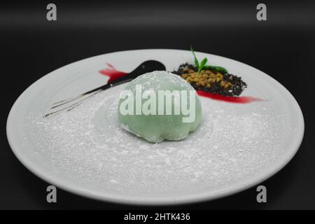 Ein traditionelles japanisches Dessert Mochi mit grünem Tee Sorbet, Gelatine aus Reis in einem verzierten Teller mit Zuckerpulver auf schwarzem Hintergrund. Stockfoto