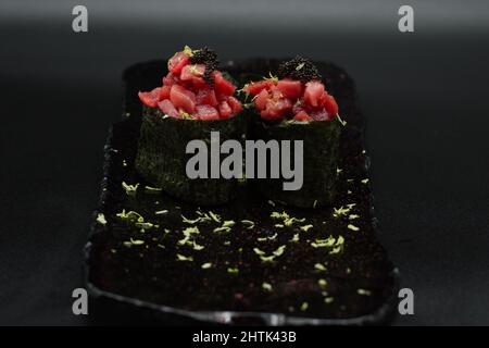 Traditioneller japanischer roter Thunfisch-Gunkan, zwei Stücke rohes Thunfischfilet, frisch geriebene Limette und schwarzer Kaviar auf schwarzem Teller mit schwarzem Hintergrund. Stockfoto